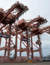 Three containers hang from cranes at Terminal 46 in Seattle. The middle container has a “Welcome to the Pacific Northwest” message to FIFA World Cup visitors, while the outside containers have the United States and Belgium flags.